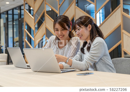 在個人計算機上帶著微笑工作的兩個女人 在個人計算機上帶著微笑工作的兩個女人 58227206