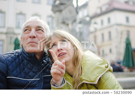 Outdoors portrait of elderly man and his young blonde wife spending time together in the ancient Outdoors portrait of elderly man and his young blonde wife spending time together in the ancient 58230090