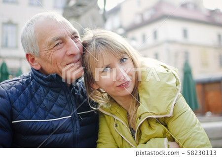 Handsome elderly man is embracing his young blonde wife spending time together outdoors in the Handsome elderly man is embracing his young blonde wife spending time together outdoors in the 58230113