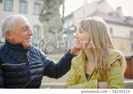 Handsome elderly man is embracing his young blonde wife spending time together outdoors in the Handsome elderly man is embracing his young blonde wife spending time together outdoors in the 58230119