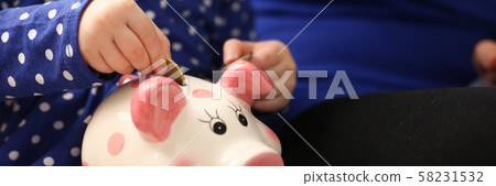 Child little girl arm putting coins into piggybank Child little girl arm putting coins into piggybank 58231532