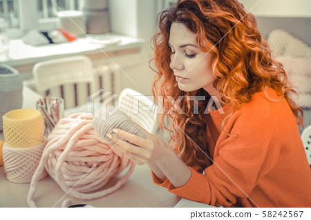 Attentive young red-haired girl staring at soft yarn 58242567