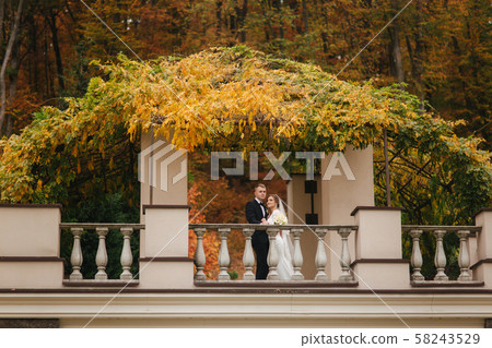 Beautiful wedding couple stand on the balcony. Stylish bride and groom in autumn weather outside Beautiful wedding couple stand on the balcony. Stylish bride and groom in autumn weather outside 58243529