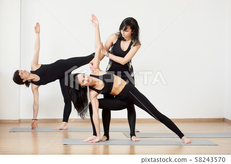 Female team exercising yoga lesson with instructor. Standing yoga poses. Trainer helping doing yoga Female team exercising yoga lesson with instructor. Standing yoga poses. Trainer helping doing yoga 58243570