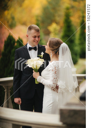 Portrait of beautiful wedding couple stand on the balcony. Stylish bride and groom in autumn weather Portrait of beautiful wedding couple stand on the balcony. Stylish bride and groom in autumn weather 58243572