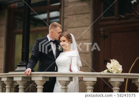 Portrait of beautiful wedding couple stand on the balcony. Stylish bride and groom in autumn weather Portrait of beautiful wedding couple stand on the balcony. Stylish bride and groom in autumn weather 58243575