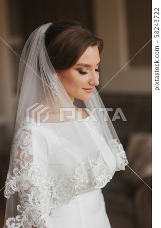 Close up portrait of beautiful bride standing by the window at home. Charming bride in white wedding Close up portrait of beautiful bride standing by the window at home. Charming bride in white wedding 58243722
