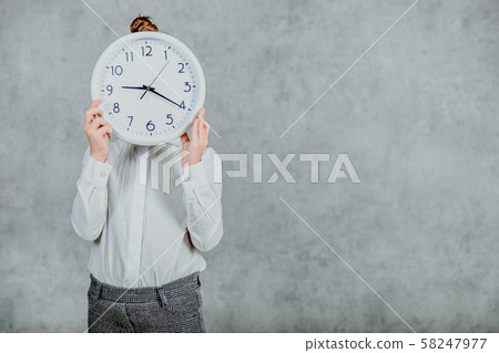 Photo of a small girl on a gray background. Modern business girl holding watch in front of her face. 58247977