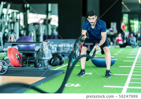 Sporty caucasian man exercising with battle ropes at the gym on green floor. Sporty caucasian man exercising with battle ropes at the gym on green floor. 58247999