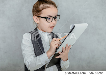 Little girl with a folder in her hands on a gray background. Dressed up as a business lady and Little girl with a folder in her hands on a gray background. Dressed up as a business lady and 58248284