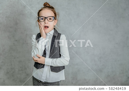Portrait of a beautiful little girl standing on a gray background. During this surprised look. Portrait of a beautiful little girl standing on a gray background. During this surprised look. 58248419