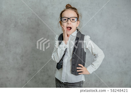 Portrait of a beautiful little girl standing on a gray background. During this surprised look. 58248421