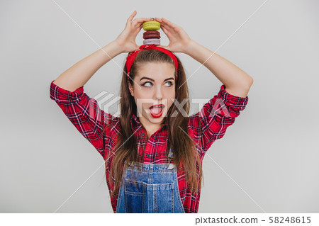 Cute young woman holding pyramid of macaroons on her head. Mouth widely opened. 58248615
