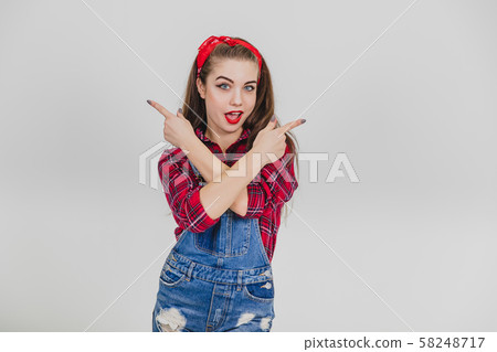 Lovely young lady standing, crossing hands, pointing up to the sides. 58248717