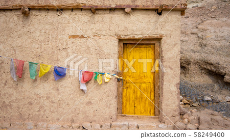 The house built from clay has a yellow entrance door. And there are colorful flags hanging at the front. An old house in the countryside of Leh, India with colorful flags hanging on the wall in front The house built from clay has a yellow entrance door. And there are colorful flags hanging at the front. An old house in the countryside of Leh, India with colorful flags hanging on the wall in front 58249400
