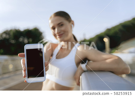 Happy athletic female showing mobile phone screen Happy athletic female showing mobile phone screen 58253915