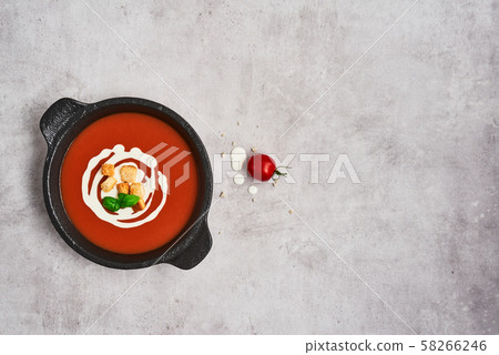 Tomato soup with cream in a black bowl on grey stone background. Tomato soup with cream in a black bowl on grey stone background. 58266246