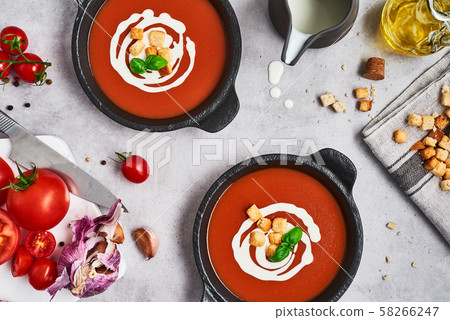 Tomato soup with cream in a black bowl on grey stone background. Tomato soup with cream in a black bowl on grey stone background. 58266247