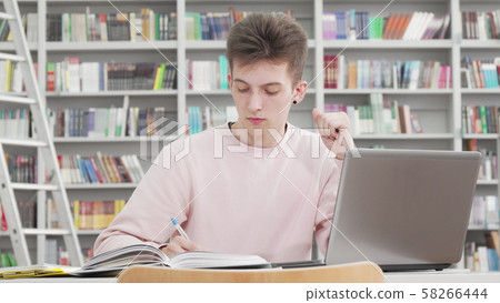 Young male student working on his laptop at college library 58266444