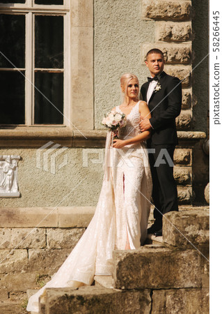 Groom and bride stand on stairs. Fashion model in elegant clothes. White long dress and stylish suit 58266445