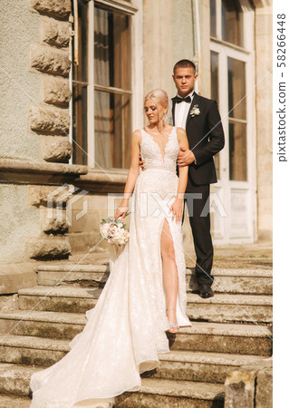 Groom and bride stand on stairs. Fashion model in elegant clothes. White long dress and stylish suit 58266448