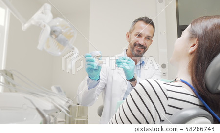 Mature male dentist teaching his patient dental care holding teeth model Mature male dentist teaching his patient dental care holding teeth model 58266743