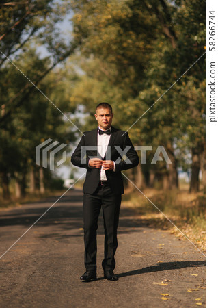 Young man walking in the park. Handsome groom in black suit Young man walking in the park. Handsome groom in black suit 58266744