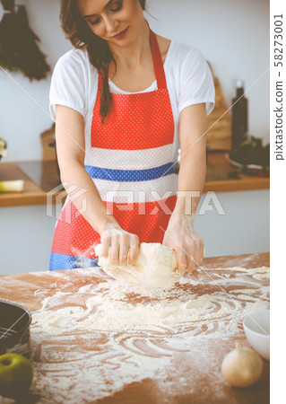 Young brunette woman cooking pizza or handmade pasta in the kitchen. Housewife preparing dough on 58273001