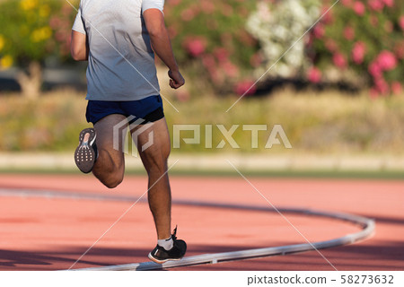Athlete running and jogging alone along a race track in stadium while out training for competition on a sunny day 58273632