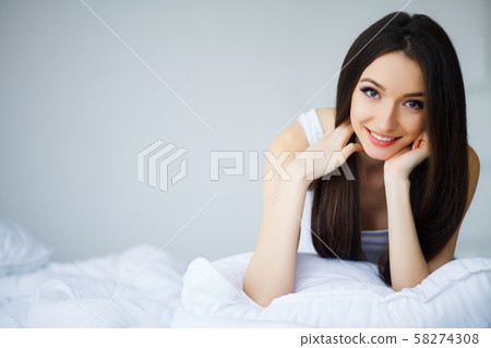 Care Concept. A beautiful young smiling brunette woman lying in white bed comfortably and blissfully Care Concept. A beautiful young smiling brunette woman lying in white bed comfortably and blissfully 58274308