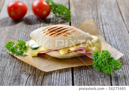 Grilled and pressed panini with ham, melted cheese, cucumber and tomatoes served on a wooden table 58275985