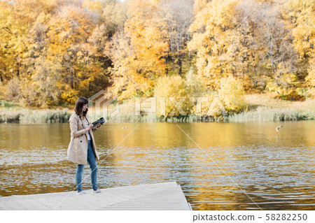 A young girl sketching near a lake in the autumn forest. 58282250