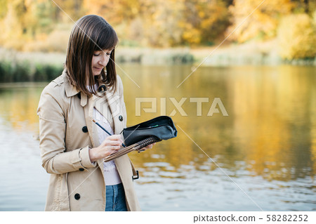 A young girl sketching near a lake in the autumn forest. 58282252