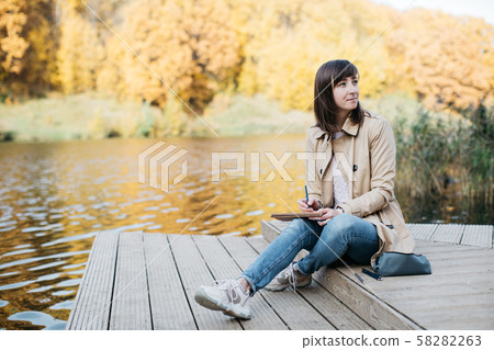 A young girl sketching near a lake in the autumn forest. 58282263