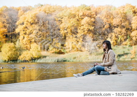 A young girl sketching near a lake in the autumn forest. 58282269