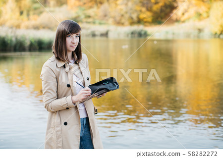 A young girl sketching near a lake in the autumn forest. 58282272