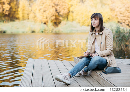 A young girl sketching near a lake in the autumn forest. 58282284