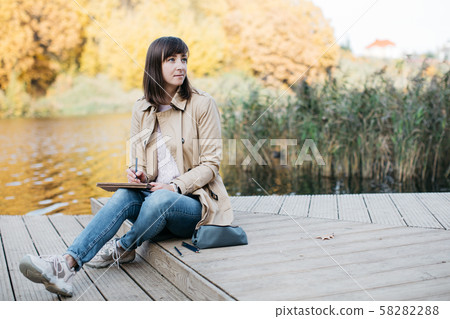 A young girl sketching near a lake in the autumn forest. 58282288