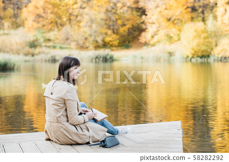 A young girl sketching near a lake in the autumn forest. A young girl sketching near a lake in the autumn forest. 58282292