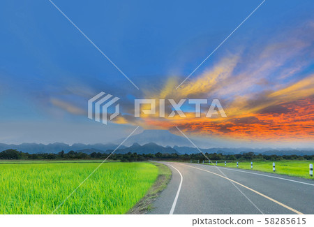 Silhouette the sunrise with the road, green paddy rice field, the beautiful sky and cloud, Thailand fuji mountain, by the beam, light and lens flare effect tone. Silhouette the sunrise with the road, green paddy rice field, the beautiful sky and cloud, Thailand fuji mountain, by the beam, light and lens flare effect tone. 58285615