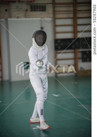 A young woman fencer standing in the fight pose holding a sword 58287988