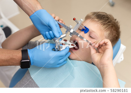 Young boy holding orthodontic arch while his dentist sets it up correctly 58290181