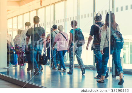 Back view of passengers and traveling luggage walking the airplane boarding corridor from the terminal to the plane. 58290323