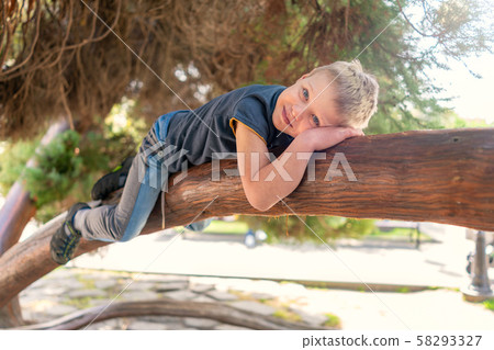 The boy lies on a thick branch of old tree like a 58293327