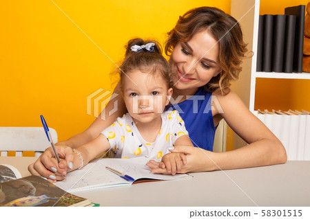 Mother with daughter studying together sitting at the table at home isolated. 58301515
