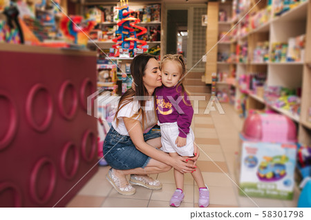 Cute little girl with her mom go into toy store. Happy kid choosing toys with mother. Mom and 58301798