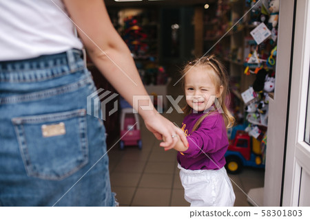 Cute little girl with her mom go into toy store. Happy kid choosing toys with mother. Mom and Cute little girl with her mom go into toy store. Happy kid choosing toys with mother. Mom and 58301803