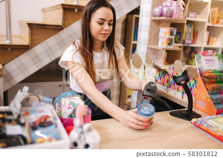 Young caucasian female woman cashier in toy store. Woman use cashier counter in kids mall Young caucasian female woman cashier in toy store. Woman use cashier counter in kids mall 58301812
