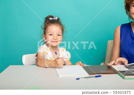 Cute little girl sitting at the desk with pen and mother near. 58301975