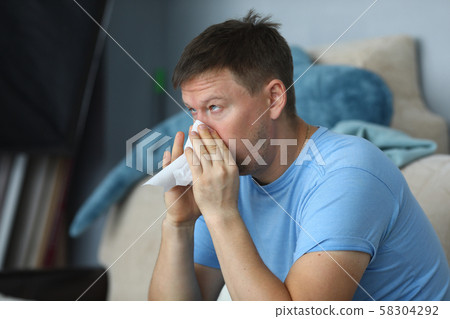 Man blowing his nose in a napkin while sitting 58304292